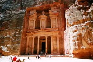 *Petra*

Dear tourists, please pay your attention to:

– To enter Petra – you do NOT need an Egyptian visa

– The excursion is conducted on the night from Tuesday to Wednesday and from Friday to Saturday

Excursion program “Petra one day trip to Jordan from Sharm El Sheikh”:

– Our guide will pick you up at your hotel gate around 1:30 am and you will travel to the Egyptian city of Taba.

The distance from Sharm El Sheikh to Taba is 190 km, arrival in Taba is expected around 06:00 in the morning.
– From the Taba you will be transported by ferry to the port of the Jordanian city of Aqaba.

The crossing by sea will take up to 1 hour. Moreover, you will be sailing in the so-called Gulf of Aqaba, which connects 4 countries: Jordan (city of Aqaba), Israel (city of Elaith), Saudi Arabia and Egypt.
– Estimated landing at the port of Aqaba is expected at 8:30 am. Our guide will meet you there, and together with him by bus you will go to the city of Petra passing through the Wadi Rum desert.

– Siq Canyon

The main part of the excursion will begin upon arrival at the Siq Canyon. You will need to walk along winding paths between the rocks for about 1200 meters. Nature has endowed the rocks in this place with an iridescent red-pink color. Finally, when you reach the end of the canyon, around one of the turns you will see a stunning view of Al Khazneh carved into the rock.
– El Khazne

– translated from Arabic – “treasury”, a Nabatean temple from the Hellenistic era. According to the legend, it was formed when the Egyptian pharaoh who was pursuing Moses created this temple with the help of magic to hide his treasures in the highest urn. Even today you can see on it traces of shots from the Bedouins, who at one time tried to get the treasures from the urn. But in fact, it turned out that the urn was carved entirely from sandstone (sedimentary rock). There is also a version that the temple was built by the Nabatean king Aretas IV Philopatris as his personal tomb. The facade of the building is 40 meters high and 25 meters wide, at the entrance there are statues of the mythological twins – Castor and Pollux, but over time many of the facade sculptures were lost. According to legend, two figures of eagles located on the roof of the building carried away the soul of the deceased.
In addition, you will be able to see the ancient amphitheater for 8,000 people, Roman colonnades and a Vyzantine church.
And it was here that part of Indiana Jones and the Last Crusade, one of the highest-grossing films, was filmed, grossing $495 million. Therefore, you will touch not only ancient history, but also the history of modern cinematography. And of course, Indiana Jones fans come here to experience part of the filming of the film live.
– Lunch time

Around 15:00, lunch will be waiting for you at a 5* hotel.
– After lunch, at approximately 17:00, we will return to the city of Aqaba for a short sightseeing tour. And at 18:00 we will take a ferry from the port of Aqaba back to the port of Taba.

Expected time of arrival at your hotel in Sharm El Sheikh is approximately 00:00.
The price of the excursion includes:

– Transfers
– Ferry tickets
– Visa to Jordan
– All customs costs
– Lunch
– All entrance fees
– Professional guide
The price of the excursion does not include:

– Beverages
– Excursion to a mountain canyon by camel, carriage or donkey
What you need to take with you:

– Passport (required!)
– Comfortable, seasonal clothing and shoes. Please note that the bus is air conditioned, so it is better to take a jacket with you
– Headdress
– Sunglasses
– Packed rations (order 12 hours before travel at your hotel reception – it’s free)
– Drinking water
– Photo and video devices
– Money for personal expenses